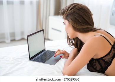 Side View Portrait Of A Woman In Sexy Lingerie Lying On The Bed With Laptop Computer