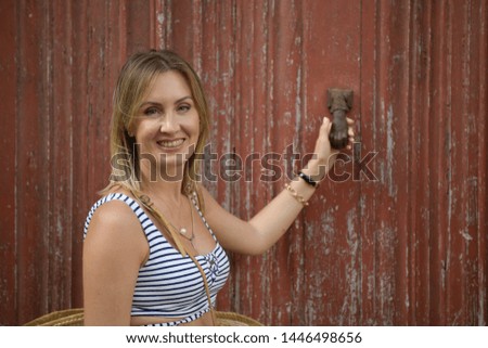Side view portrait of a woman smiling, looking at camera and holding on to a doorknob on a worn red wooden door background