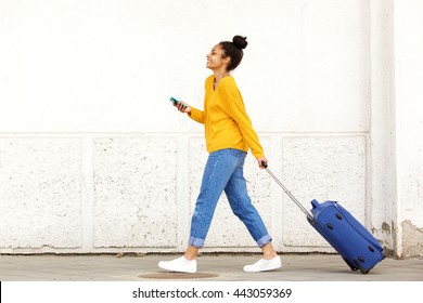 Side view portrait of woman traveler with luggage and mobile phone on city street
