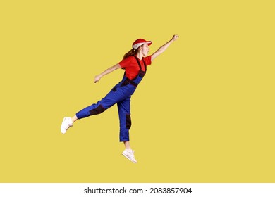 Side view portrait of woman worker flying to do her work like superhero, fast and high quality service, wearing work uniform and red cap. Indoor studio shot isolated on yellow background. - Powered by Shutterstock