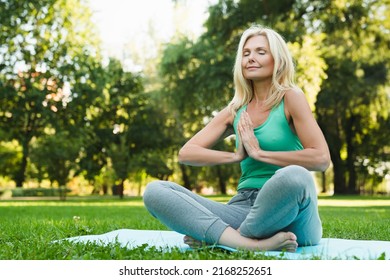 Side view portrait of a yoga on fitness mat in green public park forest. Mature beautiful woman practicing meditation relaxing feeling zen-like - Powered by Shutterstock