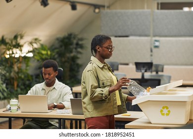 Side view portrait of young African-American woman putting paper cup into waste sorting bin in office, copy space - Powered by Shutterstock