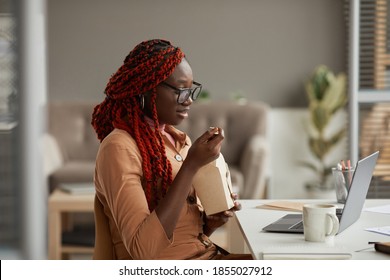Side View Portrait Of Young African-American Woman Eating Takeout Lunch And Looking At Laptop Screen While Enjoying Work Form Home Office, Copy Space