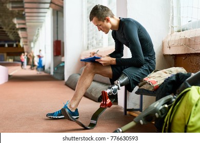 Side view portrait of young amputee athlete relaxing on bench in gym and writing something, copy space - Powered by Shutterstock