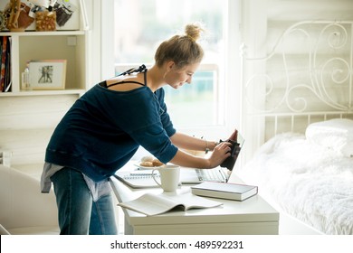 Side view portrait of young beautiful happy smiling casual woman wiping laptop screen, doing housework in her room. Indoors image