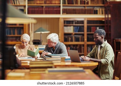 Side view portrait of young black man using laptop while studying college library with people in background - Powered by Shutterstock