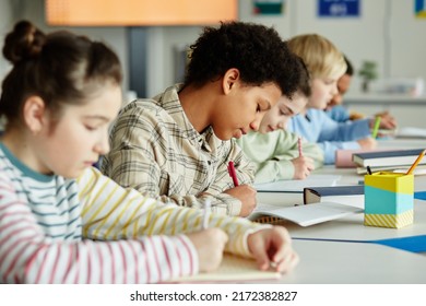 Side view portrait of young black girl taking test in school classroom with group of children sitting in row - Powered by Shutterstock