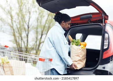 Side View Portrait Of Young Black Woman Putting Grocery Bag In Car Trunk At Supermarket Parking Lot, Copy Space