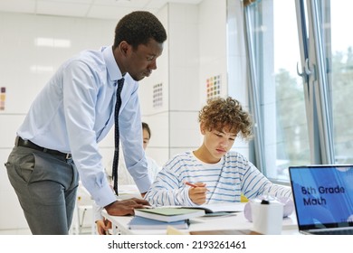 Side View Portrait Of Young Black Teacher Helping Boy In School Classroom