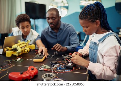 Side view portrait of young black girl building robots with male teacher in background during engineering class at school