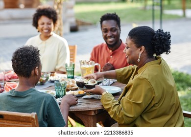 Side view portrait of young black woman serving healthy food to family while enjoying dinner together outdoors - Powered by Shutterstock