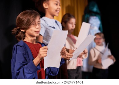 Side view portrait of young boy rehearsing lines standing on stage in school theater in row with children actors - Powered by Shutterstock