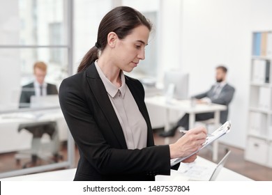 Seitenbild der jungen Geschäftsfrau, die im Büro auf der Zwischenablage schreibt, Kopienraum