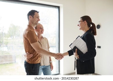 Side View Portrait Of Young Couple Shaking Hands With Real Estate Agent During Apartment Tour, Copy Space