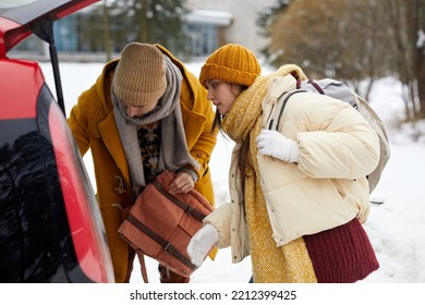 Side View Portrait Of Young Couple Unloading Car Trunk In Winter While Travelling For Christmas Holidays