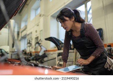 Side view portrait of young female mechanic looking under hood while inspecting vehicle in car repair shop, copy space - Powered by Shutterstock