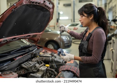 Side View Portrait Of Young Female Mechanic Checking Oil Levels While Repairing Car In Workshop, Copy Space