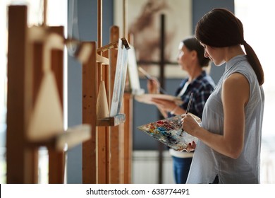Side view portrait of young female student in art class, painting oil picture on canvas