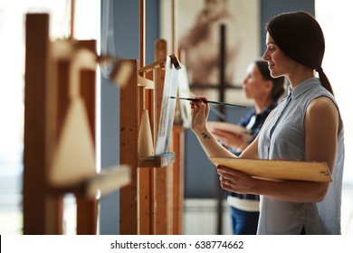 Side View Portrait Of Young Female Student In Art Class, Enjoying Painting Oil Picture On Canvas