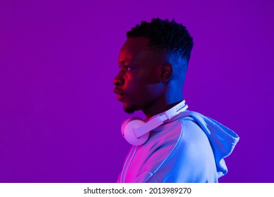 Side View Portrait Of Young Handsome African Millenial Man With Headphones In Purple Futuristic Neon Light Studio Background