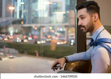 Side View Portrait Of Young Indian Business Man Sitting Near Window And Looking Over Busy City Streets. Copy Space On Window With Blurred City Scape.