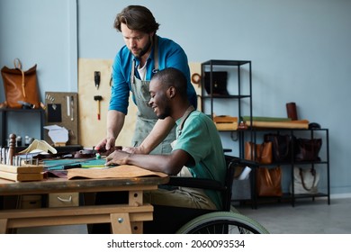 Side view portrait of young man in wheelchair learning leathermaking craft in leatherworkers workshop, copy space