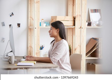 Side View Portrait Of Young Mixed Race Woman Using Computer Sitting At Desk In Home Office, Copy Space