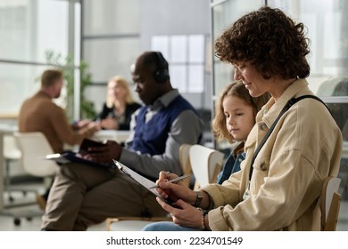 Side view portrait of young mother and daughter filling application forms while waiting in line at immigration office, copy space - Shutterstock ID 2234701549