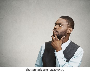 Side view portrait young, puzzled business man thinking, deciding about something, finger on lips, looking up, confused isolated grey wall background with copy space. Emotion facial expression feeling