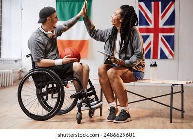 Side view portrait of young sportsman with disability high five with smiling girl in indoor basketball court copy space - Powered by Shutterstock