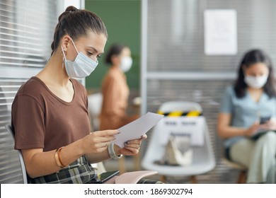 Side View Portrait Of Young Woman Wearing Mask And Holding Document While Waiting In Line In Office, Copy Space