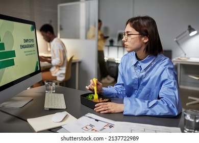 Side View Portrait Of Young Woman Eating Takeout Dinner At Desk While Working Late At Night In Office, Copy Space
