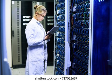 Side view portrait of young woman wearing lab coat  working with supercomputer inputting data to digital tablet standing by server cluster - Powered by Shutterstock