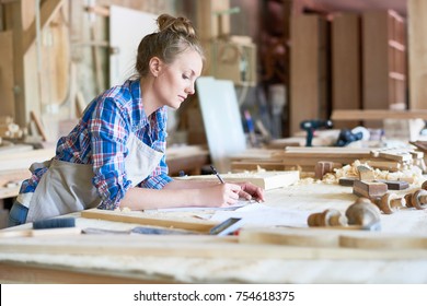 Side view portrait of young woman making notes standing at table in modern workshop, copy space