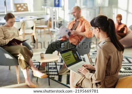 Side view portrait of young woman typing at laptop with marketing statistics on screen in company office, copy space