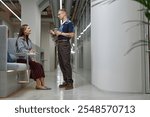 Side view of positive male businessman engaged in conversation with female coworker while collaborating in common area of modern office building, copy space