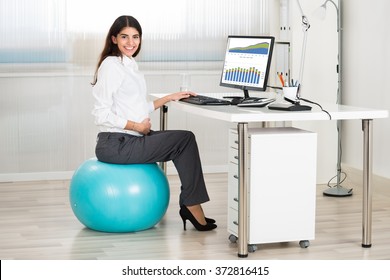 Side View Of Pregnant Businesswoman Using Computer While Sitting On Exercise Ball In Office