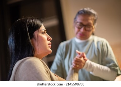 Side view of pregnant woman and blurry midwife at home. Woman in casual clothes sitting on bed, Asian doula holding hand. Pregnancy, medicine, home birth concept