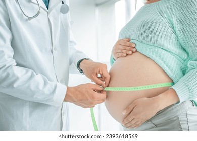 Side view of a pregnant woman middle body section exposing her belly while doctor uses a measuring tape to follow the growth of the baby at a hospital, indoors. - Powered by Shutterstock