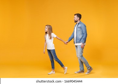 Side view of pretty bearded man in casual clothes have fun with child baby girl. Father little kid daughter isolated on yellow wall background. Love family parenthood childhood concept. Holding hands