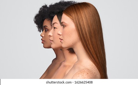 Side view of pretty diverse ladies with clean skin standing in row while representing skincare industry against gray background