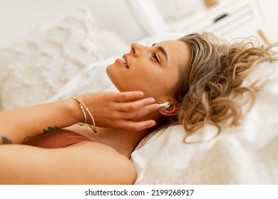 Side View Of Pretty Woman Listening Lovely Music Or Morning Audio Meditation While Lying In Bed. Warm Colors. Home Cozy Atmosphere. 