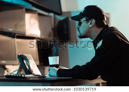 side view of prison guard sitting with cup of coffee and monitoring people in jail