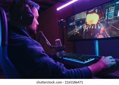 Side View Of Pro Streamer Playing Video Game Competition Use Professional Gaming Setup. Gamer Sitting On Gaming Chair Using Professional Headphones And Microphone Late At Night At Home. Cyber Sport