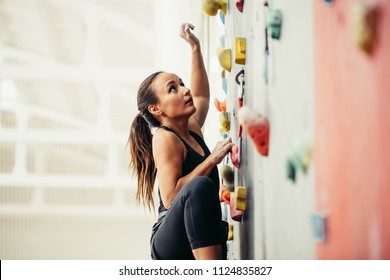 Side view of professional climber female at the rock climbing wall at the gym. Light background with copyspace - Powered by Shutterstock