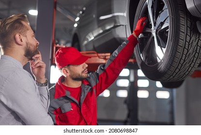 Side view of professional male technician explaining problem for customer and touching wheel of broken automobile in repair service - Shutterstock ID 2080698847