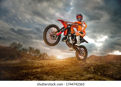 Side View of the Professional Motorcycle Rider Driving on the mountains and Further Down the Off-Road Track. It's Sunset and Track is Covered with Smoke Mist.