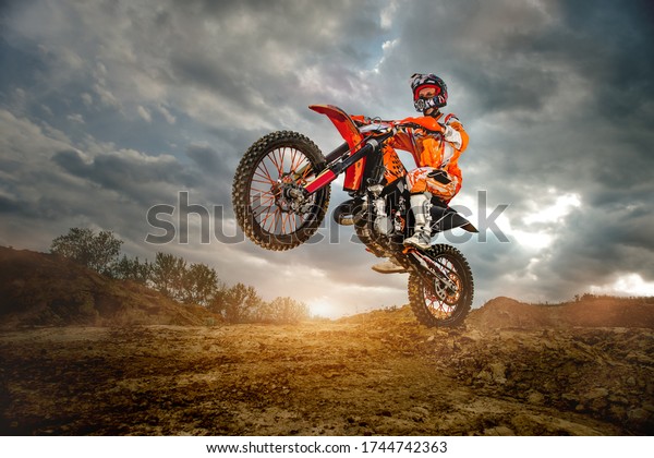 Side View of the Professional\
Motorcycle Rider Driving on the mountains and Further Down the\
Off-Road Track. It\'s Sunset and Track is Covered with Smoke\
Mist.