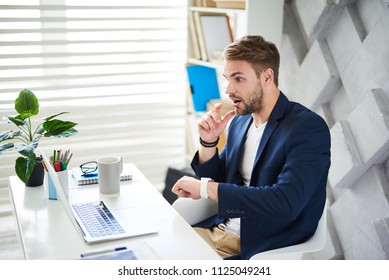 Side View Profile Of Amazed Businessman Sitting At Desktop. He Is Looking At Screen And Checking Time With Open Mouth In Astonishment