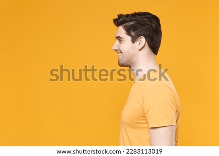 Side view profile of cheerful young smiling unshaved caucasian handsome man 20s years old wearing casual basic blank print design t-shirt look aside isolated on yellow color background studio portrait